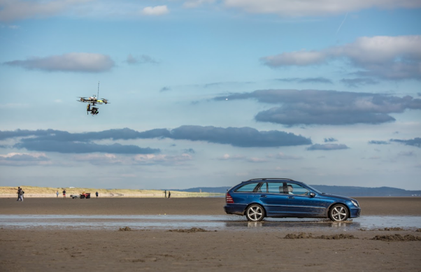 Licensed drone operator filming a car on a beach for an aerial cinematography production.